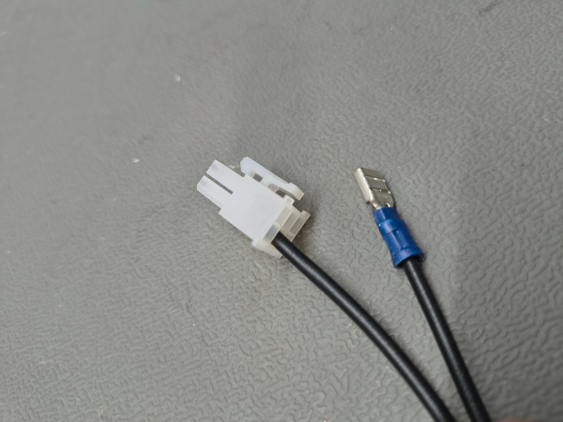 Weißer Kunststoffstecker und blauer Adapterkabelanschluss mit Metallkontakt auf grauer, strukturierter Oberfläche.